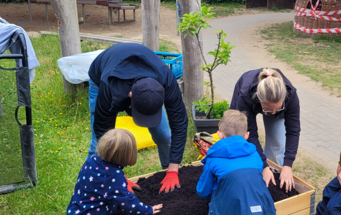 Zwei Kinder und ein Vater sowie eine Mutter füllen ein Hoch-Beet-Kasten mit frischer Erde.