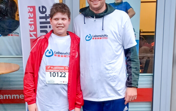 Ein Mann und ein Junge in T-Shirts der Lebenshilfe Neuss stehen beim Sommernachtslauf 2025 vor dem Lebenshilfe Center.