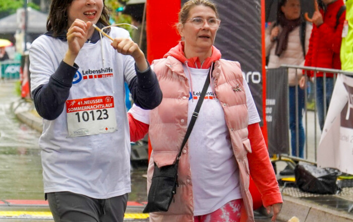 Zwei Teilnehmer des Sommernachtslauf 2025 in Neuss. Beide tragen weiße T-Shirts der Lebenshilfe Neuss.