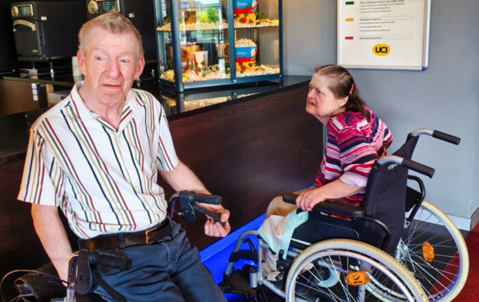Eine Frau im Rollstuhl und ein Mann sind an der Popcorn-Theke im Kino.