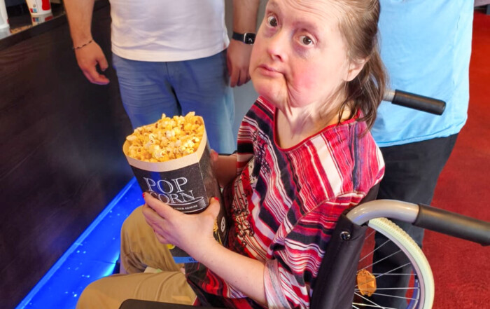 Eine Frau im Rollstuhl hält ihr Popcorn in der Hand und schaut in die Kamera.