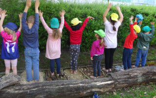 Kinder stehen in einer Reihe auf dem Barfuß-Pfad und strecken die Hände nach oben.