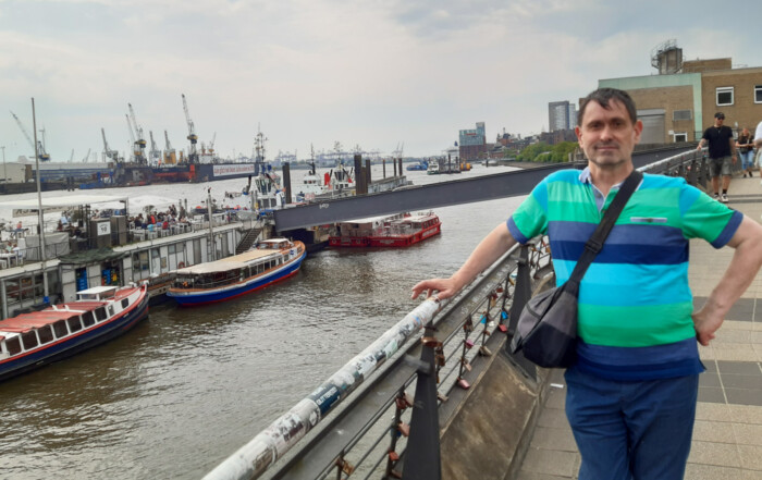 Ein Bewohner lehnt sich an ein Geländer und im Hintergrund sieht man Schiffe auf der Elbe.