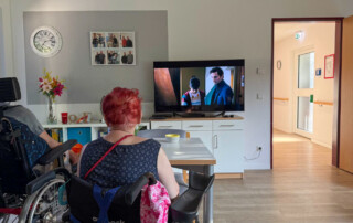Ein Bewohnerin sitzt vor dem Fernseher und schaut den Film.