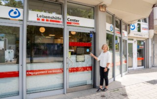 Eine Frau steht vor dem Lebenshilfe Center und zeigt auf das Refill Logo an der Eingangstür.