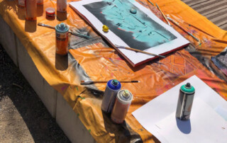 Ein Tisch mit einer Leinwand auf der Schablonen und Spraydosen liegen.