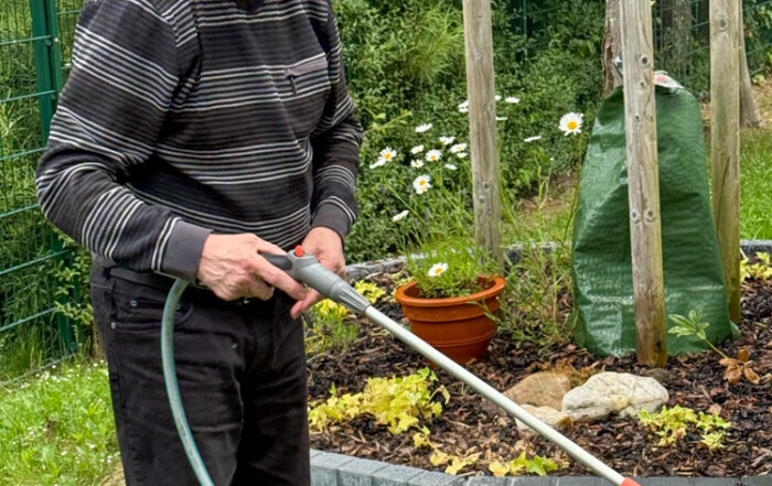 Ein Bewohner hält einen Gartenschlauch in der Hand und lächelt in die Kamera.