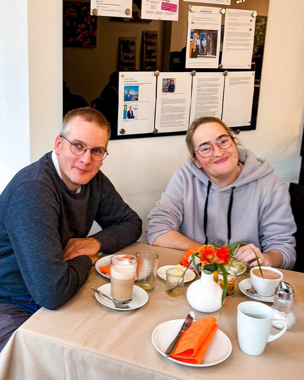 Zwei Personen sitzen am Tisch und lächeln in die Kamera.