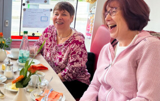 Zwei Frauen lachen gemeinsam am Tisch.
