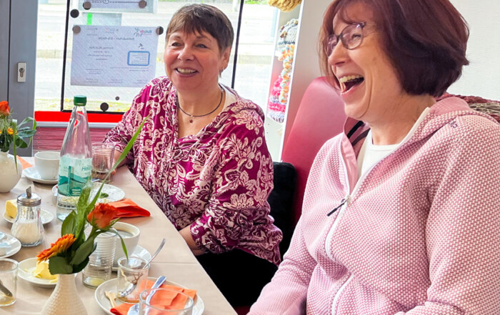 Zwei Frauen lachen gemeinsam am Tisch.