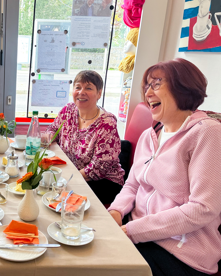 Zwei Frauen lachen gemeinsam am Tisch.