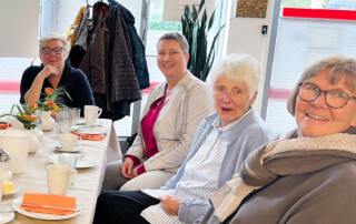 4 Frauen sitzen am Tisch und lächeln in die Kamera.