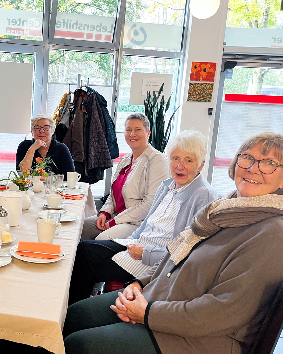 4 Frauen sitzen am Tisch und lächeln in die Kamera.