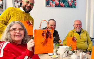 Eine Gruppe am Tisch mit orangen Tüten.