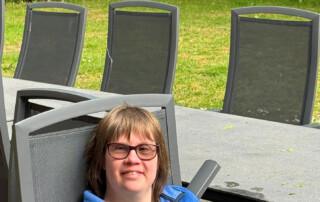 Frau sitzt im Garten. Hinter ihr drei Rehe.