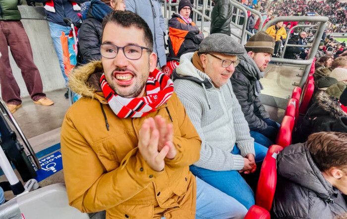 Drei Bewohner sitzen im Stadion und lächeln in die Kamera.