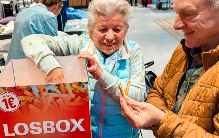 Zwei Personen kaufen sich Lose und eine Frau greift in die Losbox.