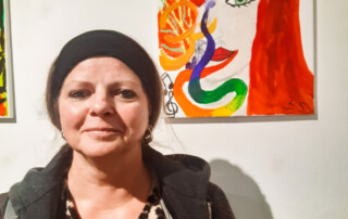 Eine Teilnehmerin steht vor ihrem ausgestellten Bild.