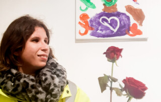 Eine Teilnehmerin steht vor ihrem ausgestellten Bild.