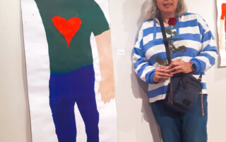 Eine Teilnehmerin steht vor ihrem ausgestellten Bild.