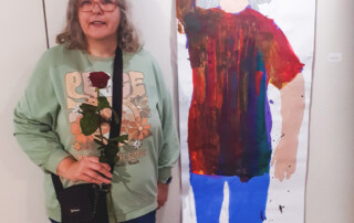 Eine Teilnehmerin steht vor ihrem ausgestellten Bild.