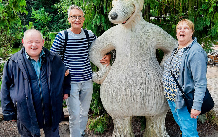 Drei Personen stehen vor eine Figur im Zoo und lächeln in die Kamera.