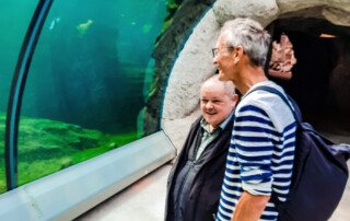 Ein Bewohner und ein Betreuer stehen vor dem Aquarium und schauen sich die Tiere an.