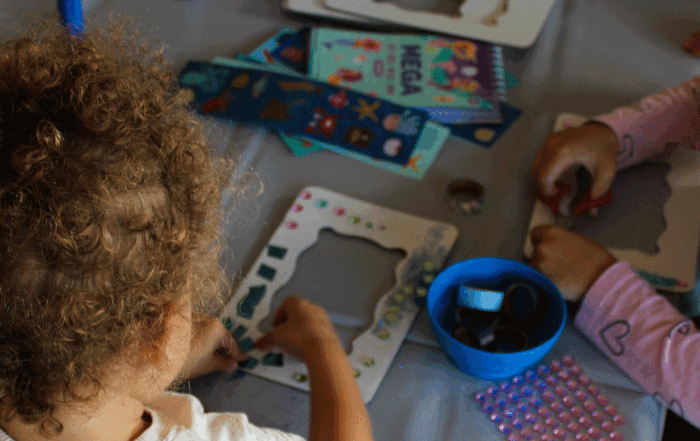 Ein Kind verziert mit Perlen einen Rahmen.