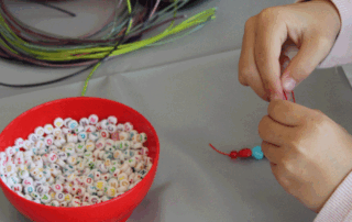 Ein Kind bastelt ein Perlenarmband.