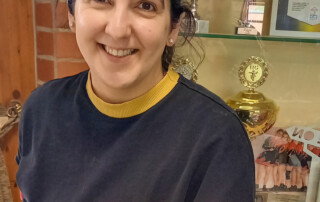 Eine Frau hält einen Teller mit einer Waffel drauf in die Kamera und lächelt.