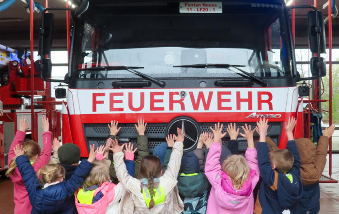 Die Kinder stehen vor einem Feuerwehr-Auto und strecken die Hände in die Luft.