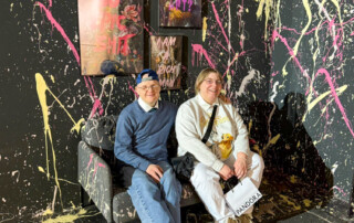 Zwei Bewohnenede sitzen auf einer Bank mit einer mit Farbe befleckten Wand.