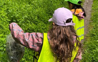 Zwei Kinder in Warn-Westen sammeln Müll im Wald.