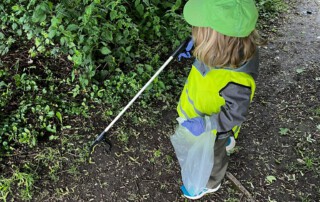 Ein Kind in Warn-Weste sammelt Müll im Wald.