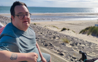 Eine Person sitzt am Strand und lächelt in die Kamera.