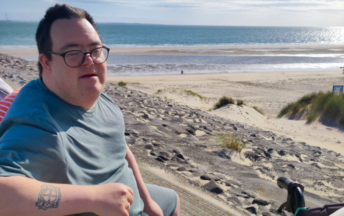 Eine Person sitzt am Strand und lächelt in die Kamera.